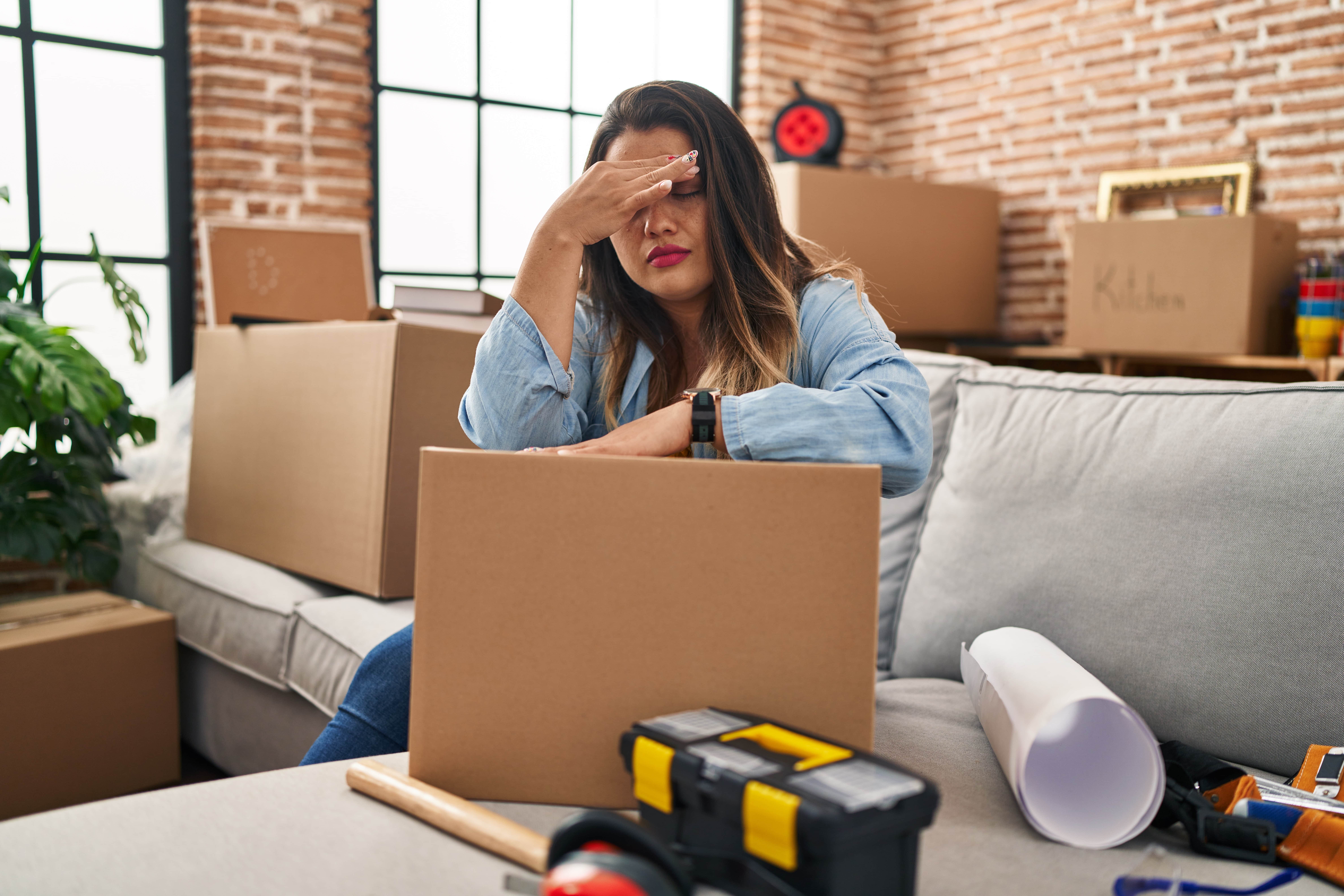 Young plus-size woman sitting on floor surrounded by moving boxes, looking stressed while packing for a move